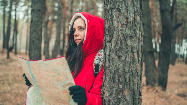 A traveling woman with map in woods. A portrait of the pretty woman with a backpack, standing near a tree in a cold weather