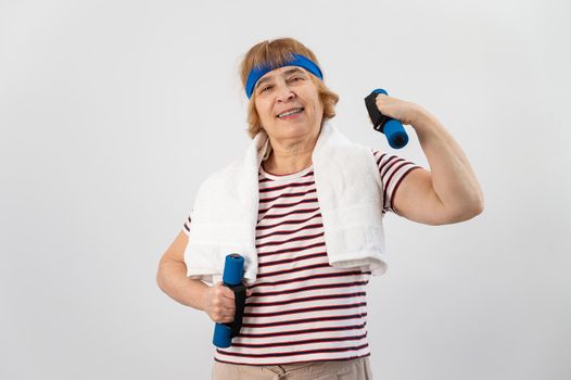 An elderly woman with a blue bandage on her head trains with dumbbells on a white background.