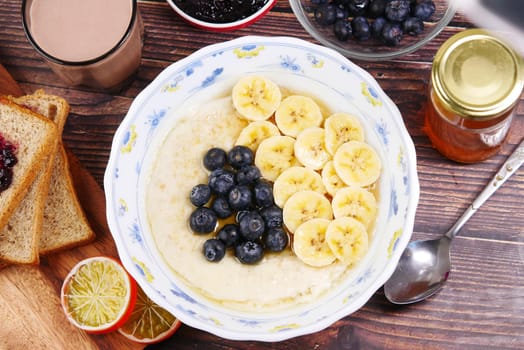 a bowl of oats, berry, banana and honey on table .
