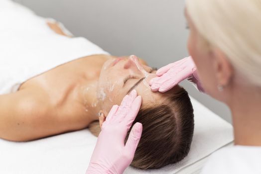 Young beautician or dermatologist doing manual facial cleansing for a woman in a beauty salon. Spa facial massage. Beautiful woman receiving facial massage in a beauty salon. The beautician makes cosmetic procedures to a female client.