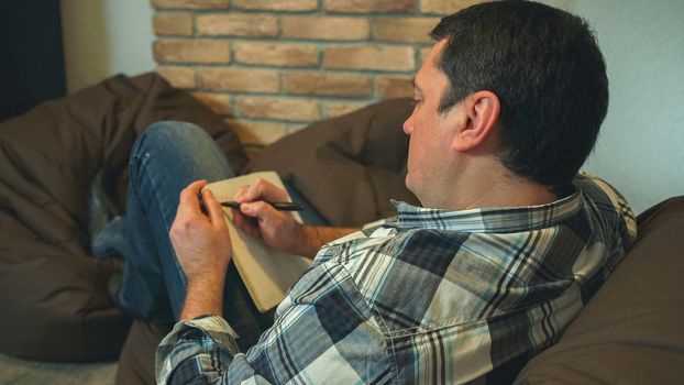 Men rest on the sofa and make notes. Writing in the notebook