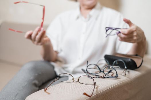 An elderly Caucasian woman chooses glasses from her home collection.