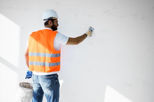 Plasterer in workwear smoothing wall surface of building indoors, close up