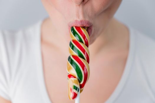 Close-up portrait of a woman sucking a long lollipop against a white background. Blowjob simulation.
