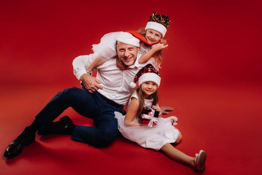 Portrait of a happy family in a Christmas hat on a red background. Dad and daughters at Christmas.