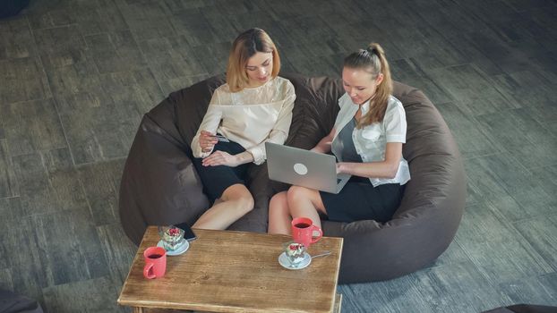 Two attractive blondes make an online purchase, one holding a credit card, and the second makes a purchase with laptop. Soft panorama