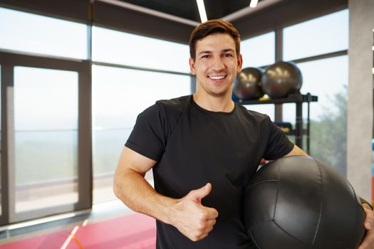 Fit young man exercising with fitness ball in a gym, close up