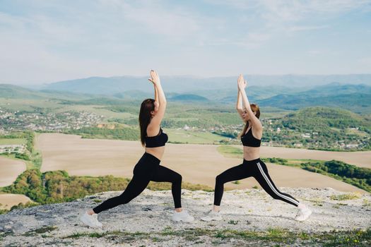 Two girls play sports on a cliff. Yoga in nature. A healthy lifestyle.