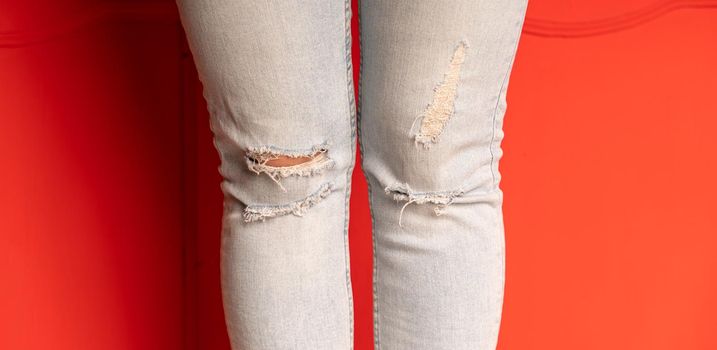 Close up of women's legs in jeans with holes on red background. Fashionable holes in jeans on unrecognizable female