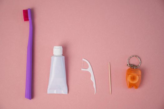 Personal oral hygiene product on a pink background. Toothbrush tube toothpaste toothpick and floss. Flat lay.