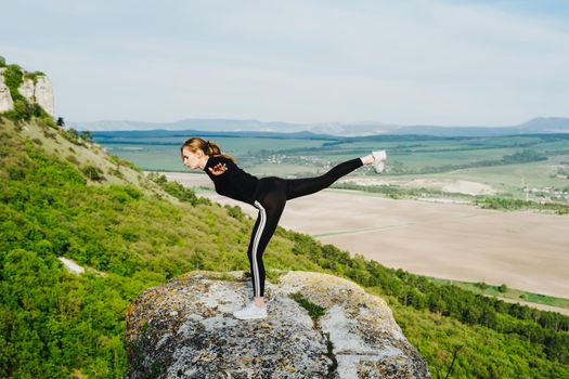 A girl in a swallow pose on the edge of a cliff. Outdoor sports.