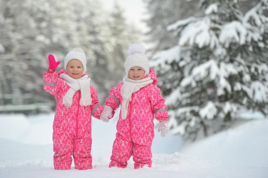 Two little twin girls in red suits stand in a snowy winter forest.