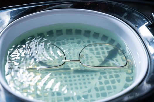 Ultrasound cleaning of glasses in solution. Optical technician repairs the frame of glasses.