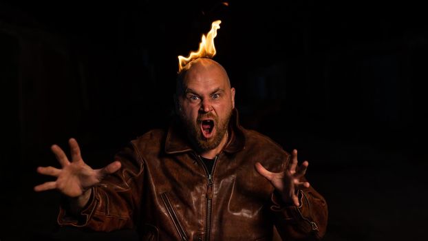 Bald man in a leather jacket with a burning head on a dark background