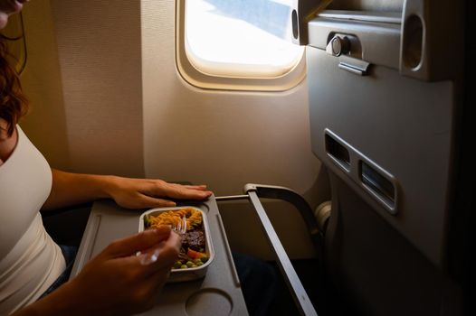 Caucasian woman flying in economy class and eating lunch from a tray table on board the plane