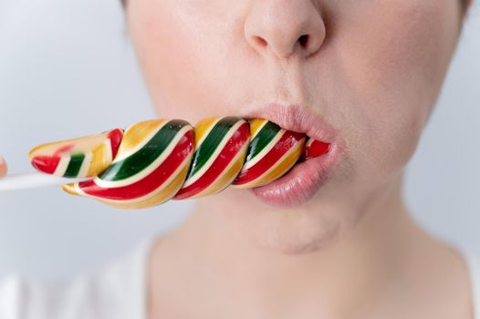 Close-up portrait of a woman sucking a long lollipop against a white background. Blowjob simulation.