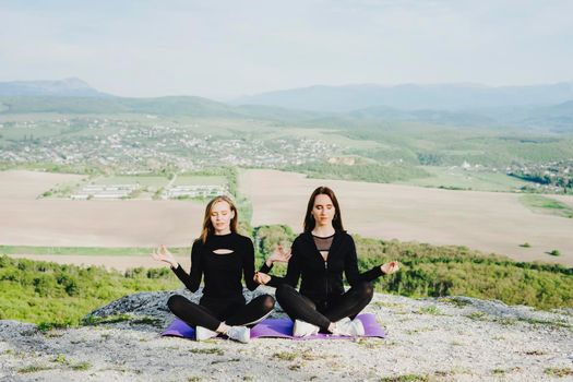Two girls sit in a lotus pose on a purple yoga mat. Outdoor sports. Sports in the mountains. Meditation.