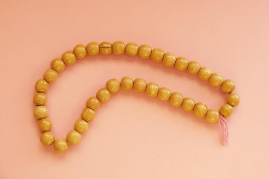 wooden rosary for prayer on a pink background.