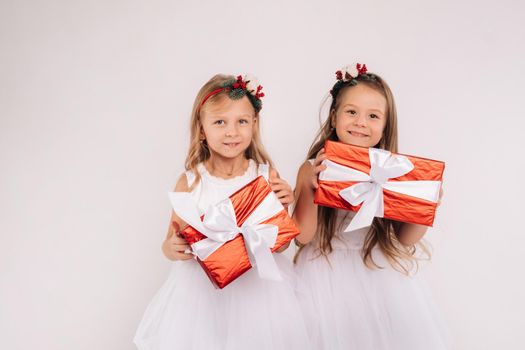 two little girls in white dresses with Christmas gifts on a white background smile.