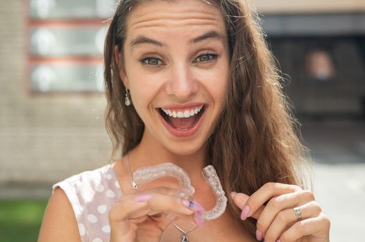 Beautiful caucasian woman holding transparent mouth guards for bite correction. Girl with silicone braces outdoors