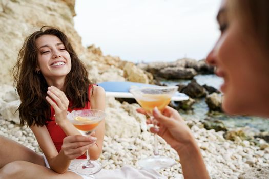 Two young female friends having a picnic on a beach drinking cocktails