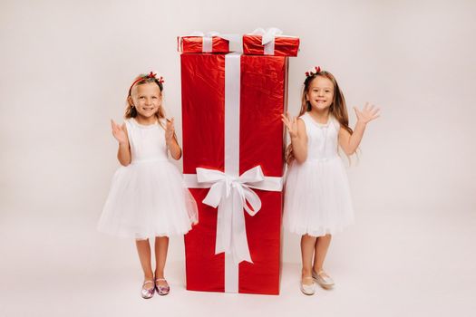 two little girls with Christmas gifts on a white background and a huge gift.