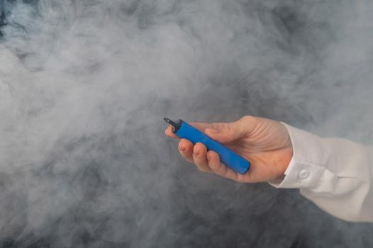 Caucasian woman smokes disposable vape on black background. Alternative device for smoking. Close-up of a female hand