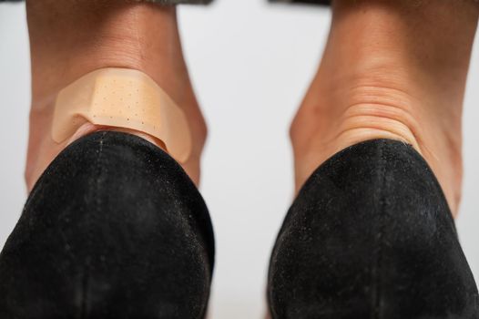 A woman in black shoes puts a plaster on a corn.