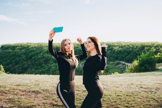 Girls in black tracksuits take selfies on a smartphone. Girls actively relax in nature.