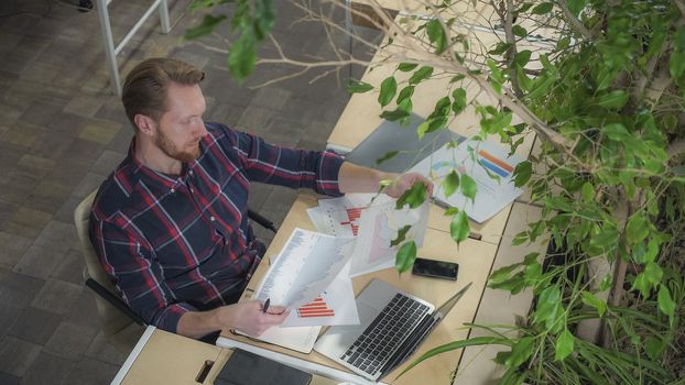 The bearded man sits in the environmental office and looks at the figures on paper. Static video