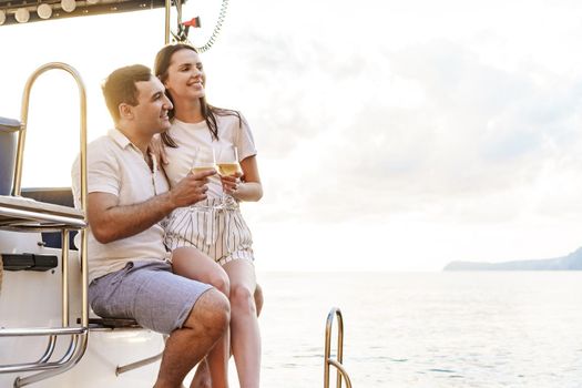 Young loving couple sitting on the yacht deck and drinking wine together