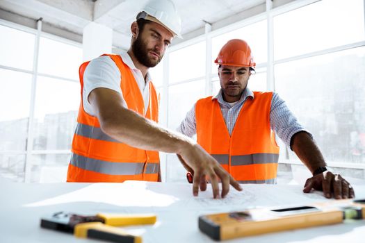 Two young engineers man looking at project plan on the table in construction site