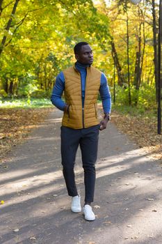 african american young man in stylish clothes walks in autumn park on sunny warm autumn day. Concept of weekend and outdoor recreation
