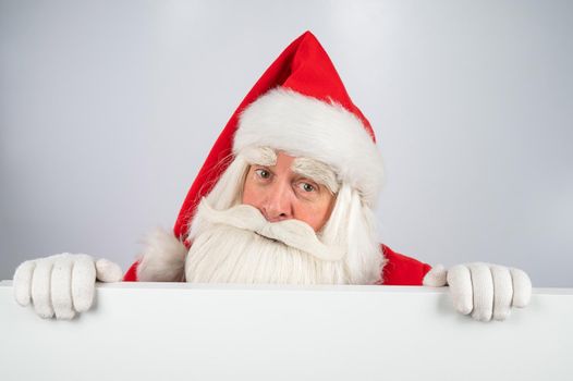 Santa Claus peeks out from behind an ad on a white background. Merry Christmas