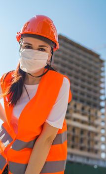 Portrait of female construction worker in medical mask and overalls on background of house under construction