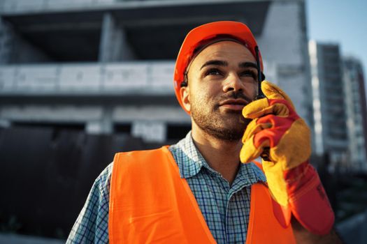 Young construction worker in uniform using walkie talkie on site, close up portrait