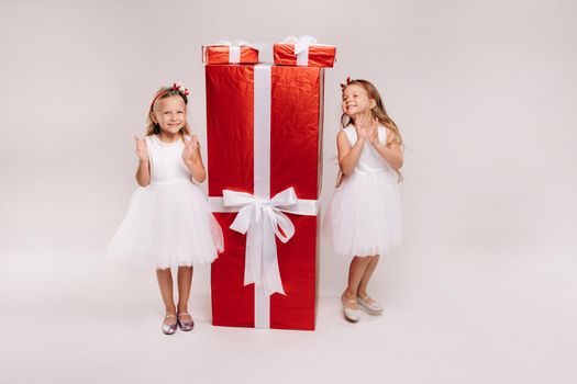 two little girls with Christmas gifts on a white background and a huge gift.