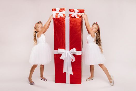 two little girls with Christmas gifts on a white background and a huge gift.