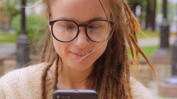 close up face young caucasian woman with dreadlocks and eyeglasses using smartphone texting message or chatting online