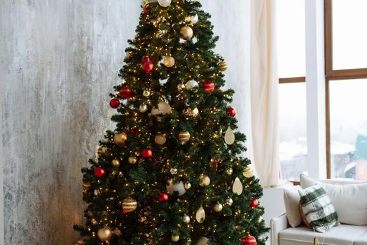 Christmas tree with red and gold balls and gold garland lights in a bright room