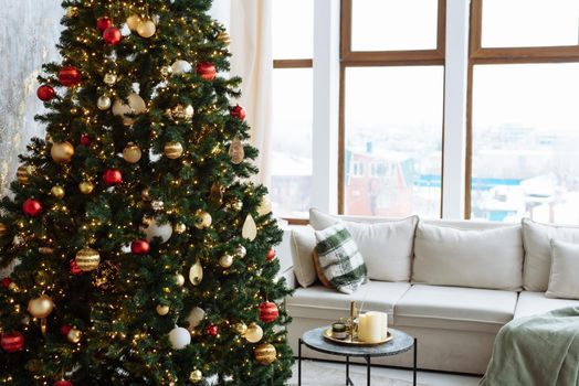 Christmas tree with red and gold balls and gold garland lights in a bright room