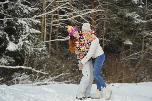 Two girls in the winter forest emotionally hug and smile.Happy women hug and Express joy.