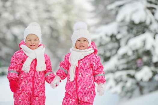 Two little twin girls in red suits stand in a snowy winter forest.