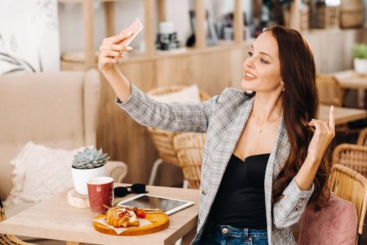 a business Girl is sitting in a cafe and taking a selfie,a Girl in a coffee shop is smiling and taking a selfie on a smartphone.