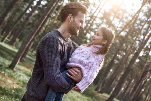 Little girl and her father in the forest. Girl is looking to the father. Young man is wearing a dark sweater, girl is in pink bright sweater
