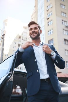 A young handsome man in a suit comes out of the car and laughs