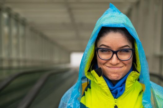 Smiling young woman in a jacket and raincoat on a travolator. Girl in protective clothing from the rain.