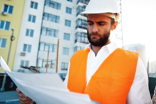Builder or architect in hardhat supervising a project, looking at blueprints, close up