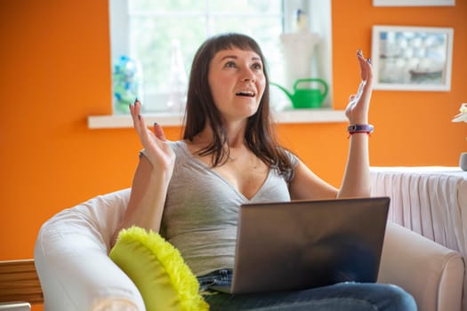 Portrait of charming, emotional, worried, nervous woman gesture with hands, looking at computer, something went wrong, can't get in time, sitting at chair.