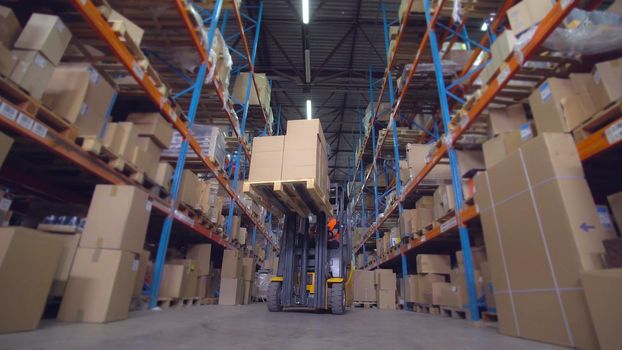 forklift operator puts boxes with goods on the metal racks. worker in storehouse driving on the special vehicle.